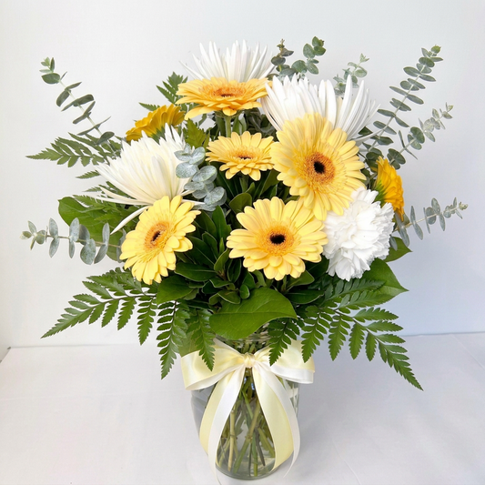 Bouquet of orange and white flowers in a clear vase with an orange ribbon on a light background. Delivery in Chilliwack Cultus Lake and Sardis.